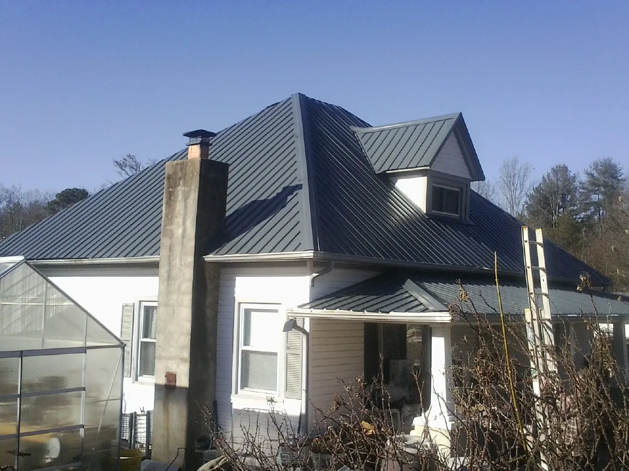 Dark blue standing seam metal roof on a white farmhouse with dormer — Slate & Tile Roof Repair by Roofing Brothers in Spanaway