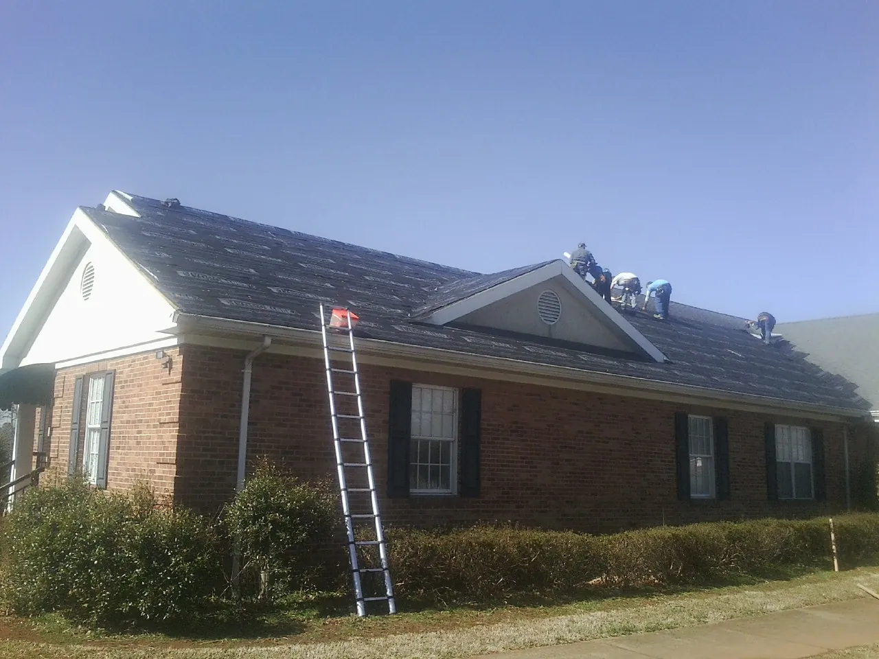 Crew tearing shingles off a brick ranch roof with a ladder set — Metal Roof Repair work by our crew in Spanaway