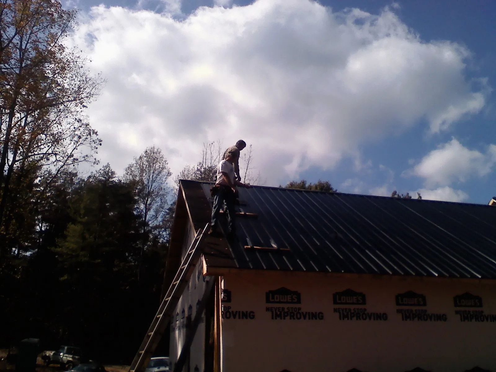 Roofer fastening dark metal panels high against a cloudy sky, from a Roof Inspection job in Spanaway